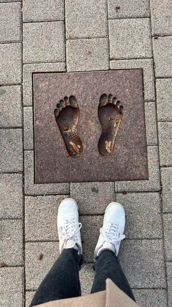 et avtrykk av føtter på en plansje i asfalten i vilnius og et par bein med hvite sko som står foran