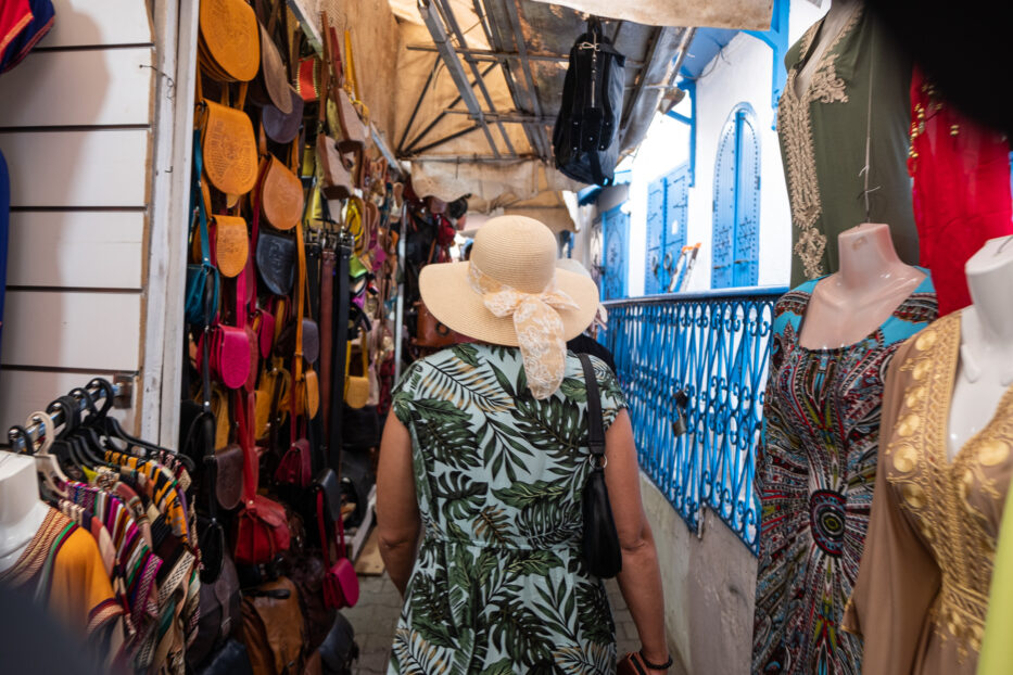 a woman in a blue dress with a hat with a bow on top walks through the medina in sidi bou said