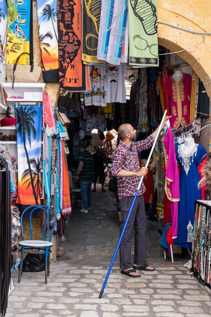 a man hangs up clothes in his shop in the medina in sidi bou said