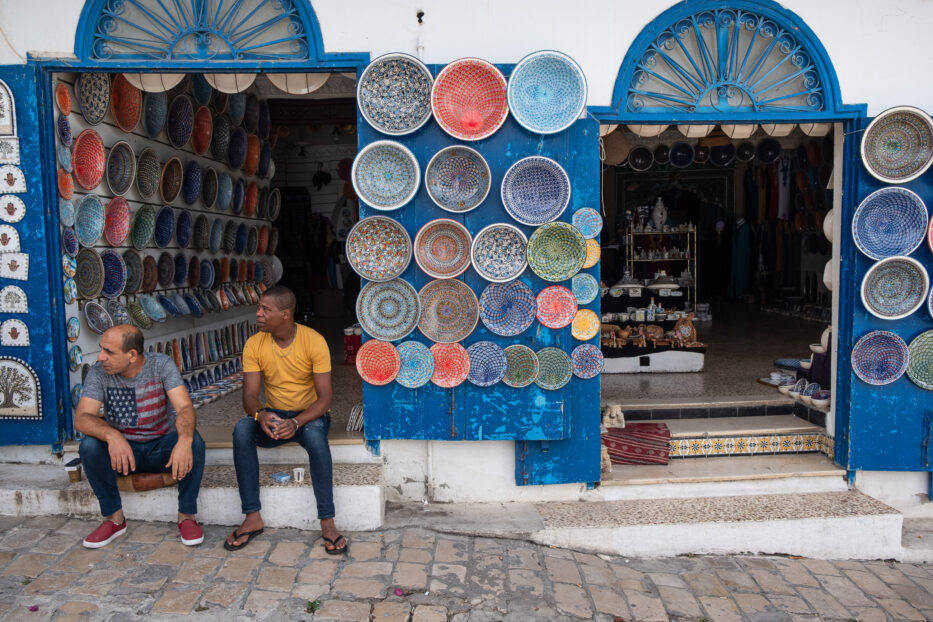 to menn sitter utenfor butikken sin med fargerik keramikk på gata i sidi bou said