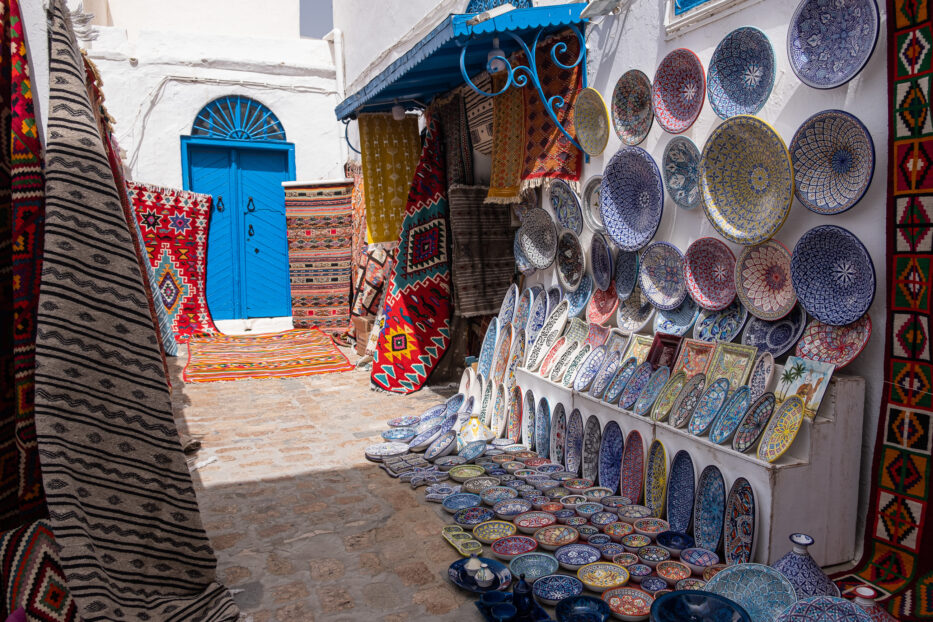 colourful ceramics and carpets placed outside a storefront in a street in sidi bou said