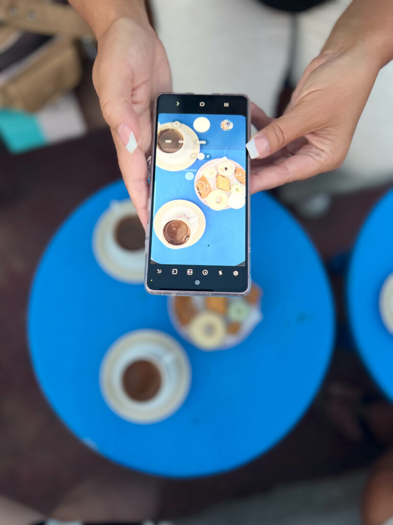 a woman taking a photo of coffee and small cakes with her smartphone at cafe des delices