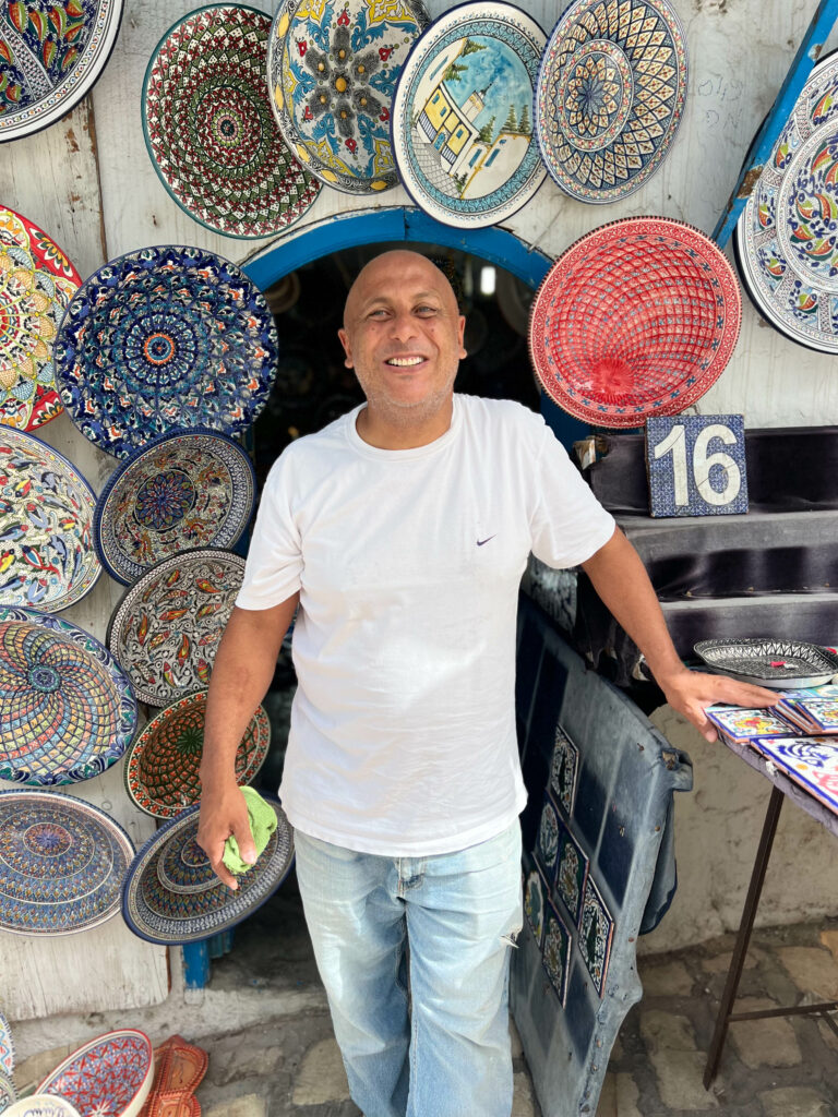 a smiling man outside his shop which sells ceramics in sidi bou said
