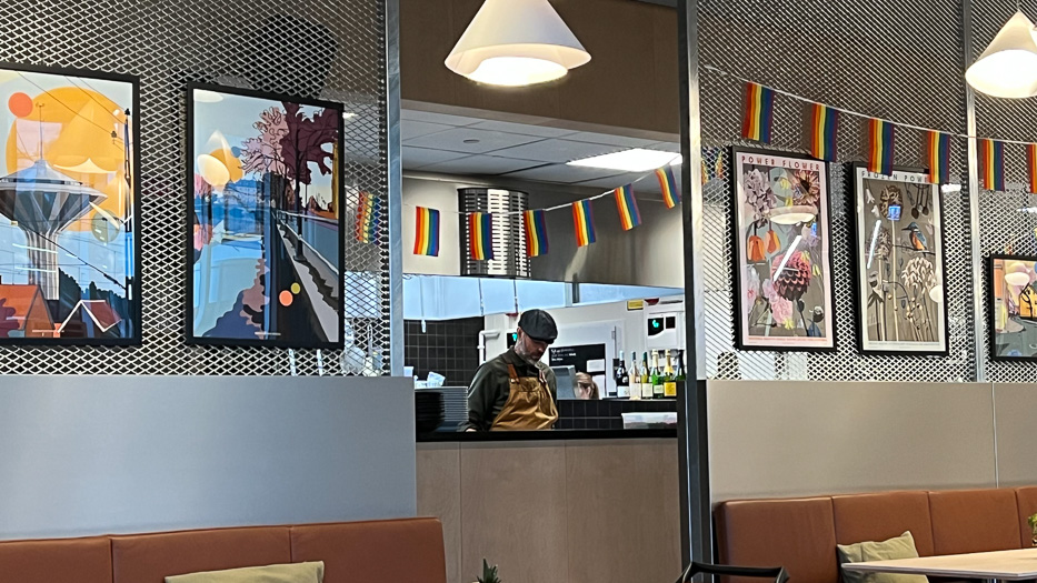 mann jobber på kulturbistron innrammet av kunstverk og pride-flagg ved disken