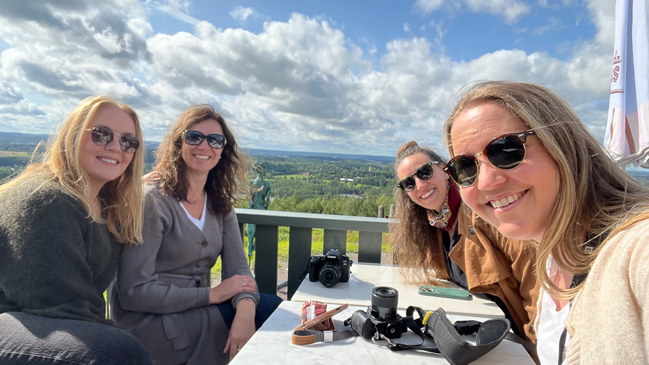 fire smilende kvinner foran et grønt landskap rundt et bord med flere kameraer og en iphone på toppen