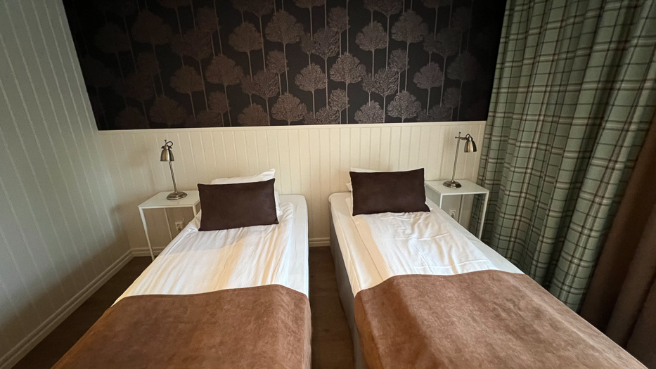 inne på et soverom på Katrinelund Gästgiveri & Sjökrog to senger med brune detaljer og tapet med trær og grønnrutete gardiner