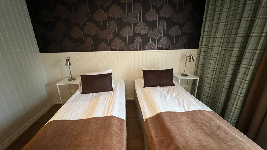 inside a bedroom at Katrinelund Gästgiveri & Sjökrog two beds with brown details and wallpaper with trees and green curtains