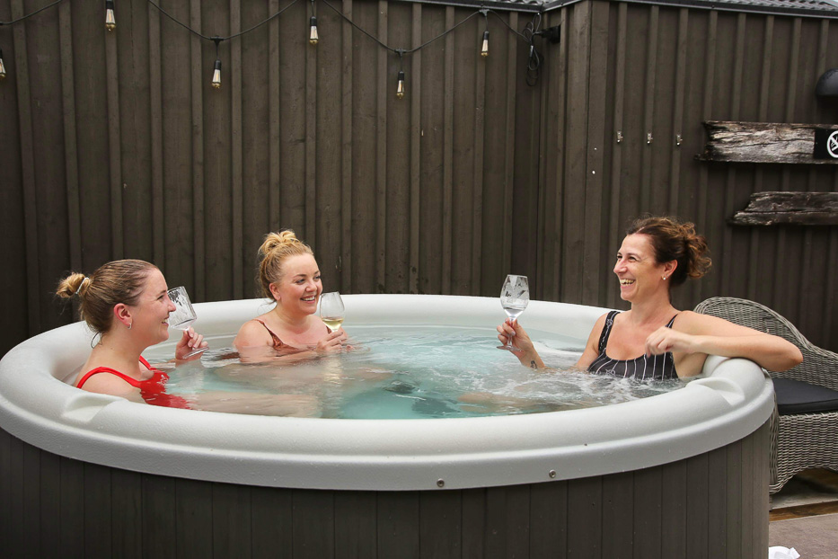 tre smilende kvinner i et boblebad på Katrinelund Gästgiveri & Sjökrog holder glass med vin i hendene