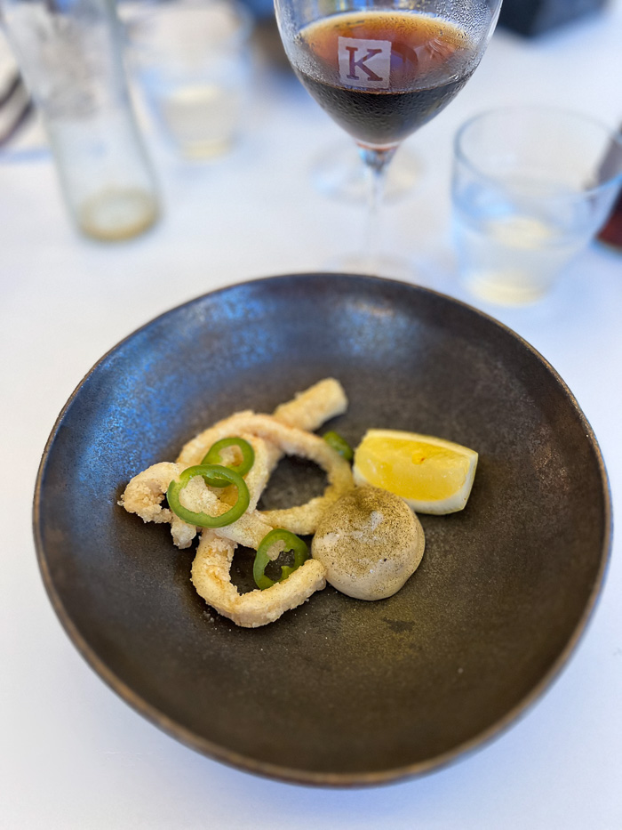 a round, brown plate with octopus, lemon and green pepper, and a glass of pepsi max in the background