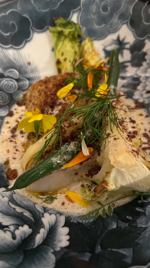 close-up of a white fish-dish with vegetables and edible flowers