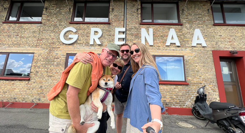 four smiling people and a dog in front of a wall saying grenaa