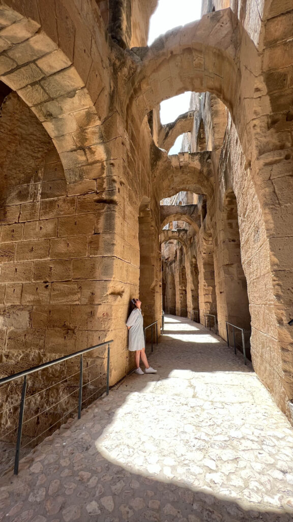 a woman standing inside the ruins of the amphiteater in el jem looking up