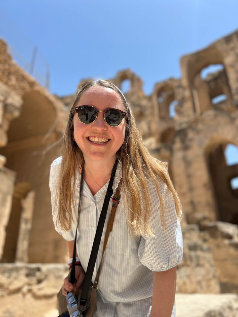 smilende kvinne med solbriller inne i amfiteateret i el jem