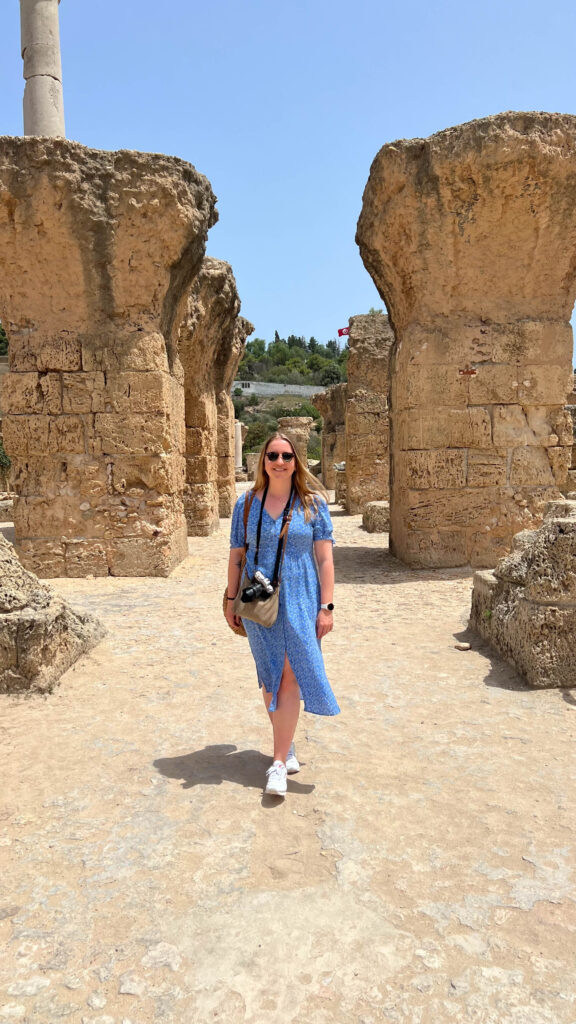 smiling woman in blue dress standing between ruins in carthage