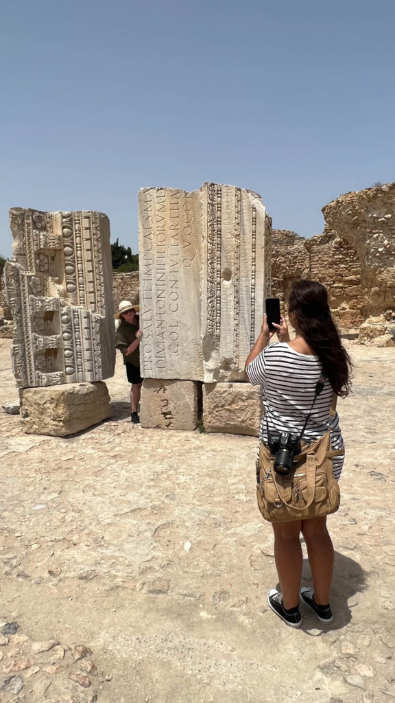a woman taking a photo with a smart phone of a woman and ruins in carthage