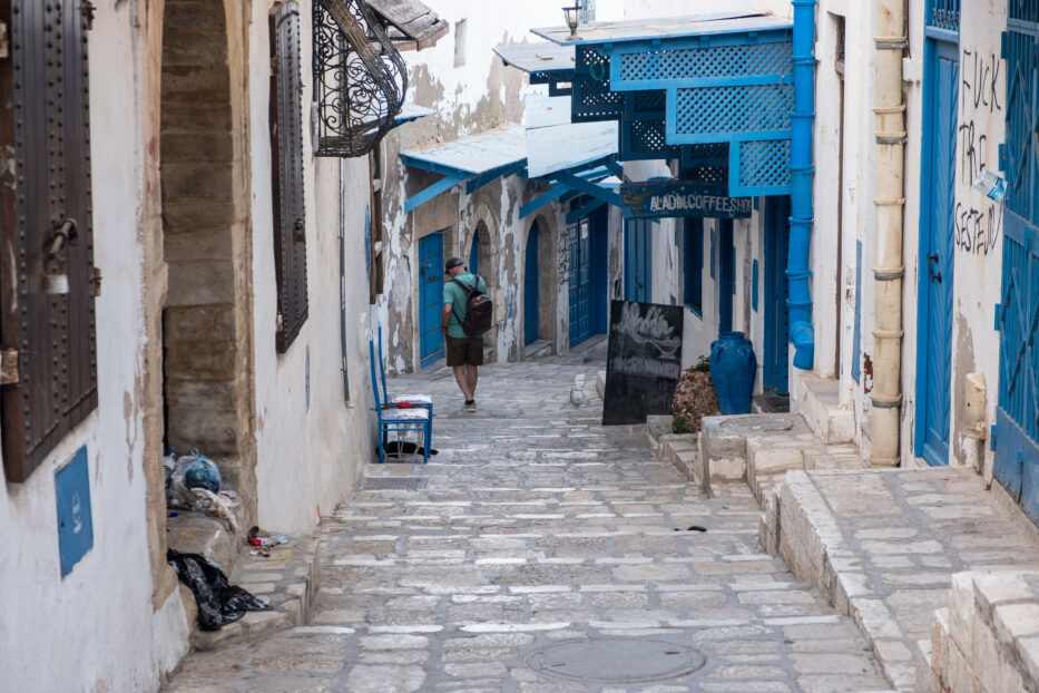 en mann går gjennom en folketom brosteinsgate med hvite hus og blå detaljer i sousse