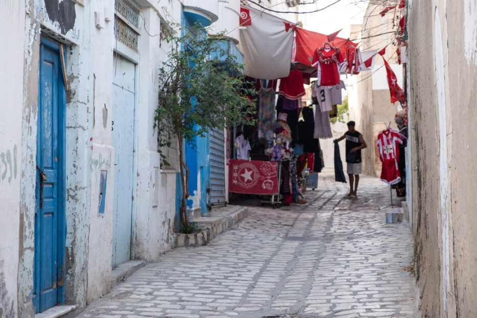 en mann ordner med klær opphengt på en snor utenfor en butikk i sousse